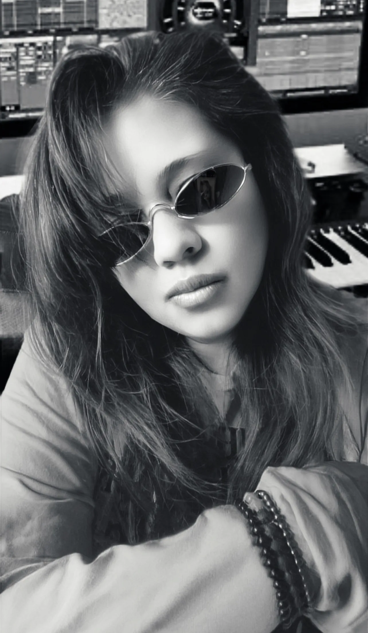 Anjalts in small sunglasses at the workstation, keyboard and mixing screens behind, black and white